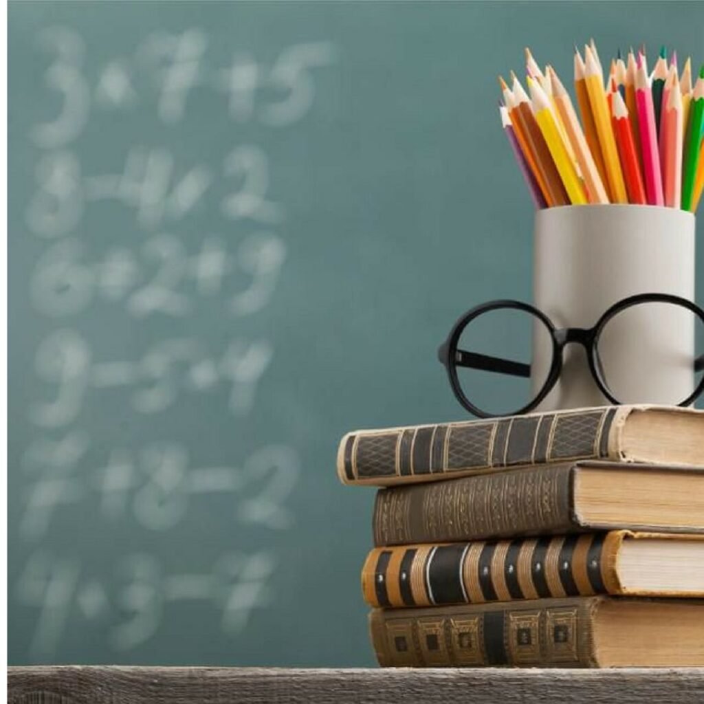 Stack of books, glasses and coloured pencils in front of a chalkboard with sums